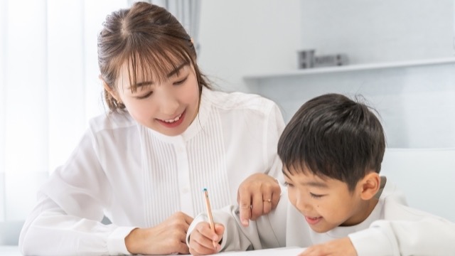 鉛筆を持つ女性と一緒に机に向かって学習する男の子